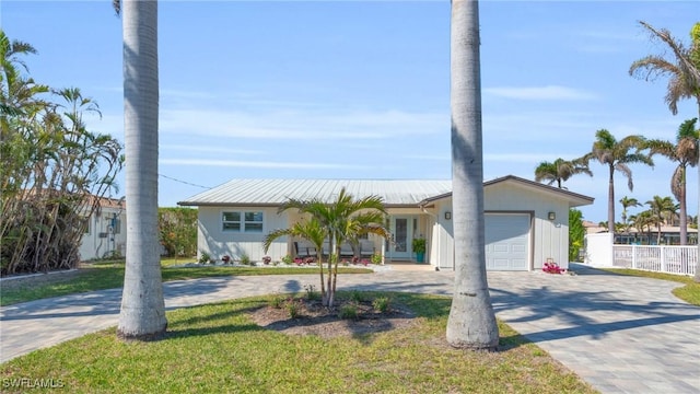 view of front facade with decorative driveway, an attached garage, a front yard, metal roof, and fence