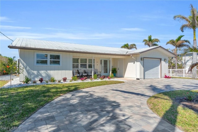 view of front of home featuring a front yard, decorative driveway, metal roof, and an attached garage