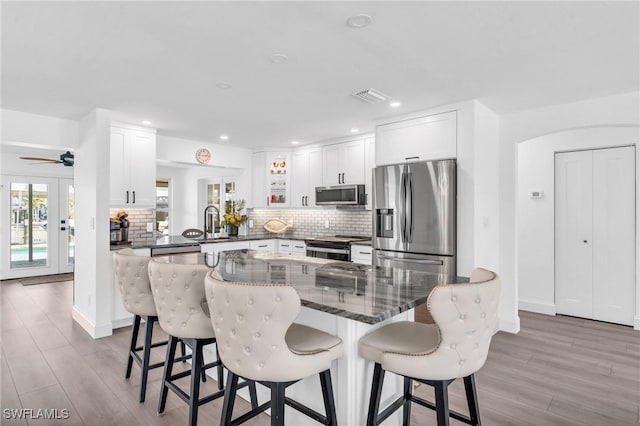 kitchen featuring glass insert cabinets, white cabinetry, a kitchen bar, and appliances with stainless steel finishes