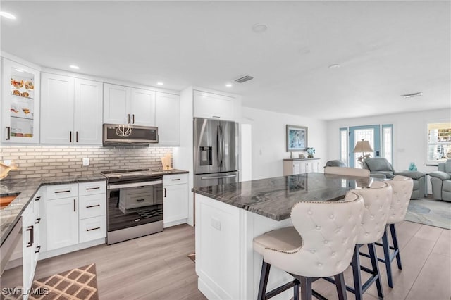 kitchen with dark stone countertops, appliances with stainless steel finishes, a breakfast bar area, and white cabinets