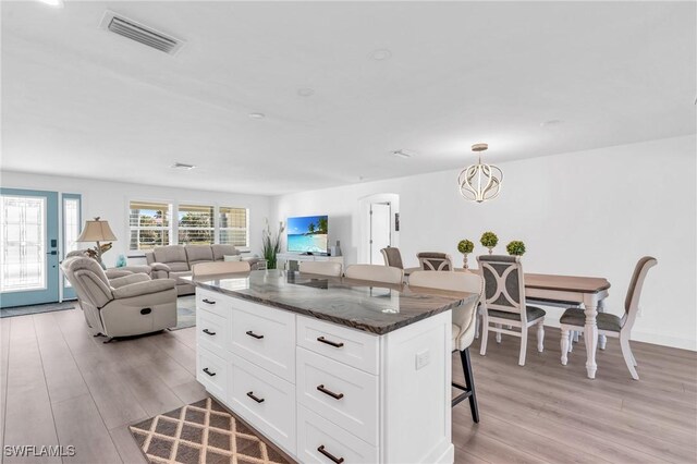 kitchen with a kitchen island, white cabinetry, a breakfast bar area, dark stone counters, and light hardwood / wood-style flooring