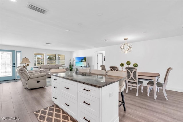 kitchen with a breakfast bar, visible vents, white cabinets, open floor plan, and a center island