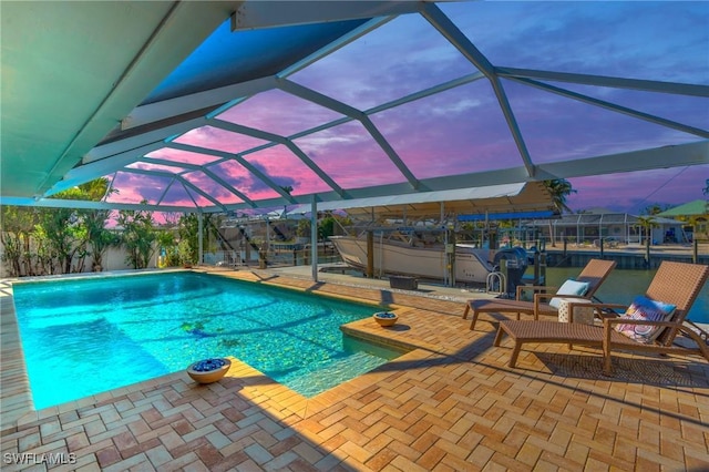 pool at dusk featuring a lanai and a patio