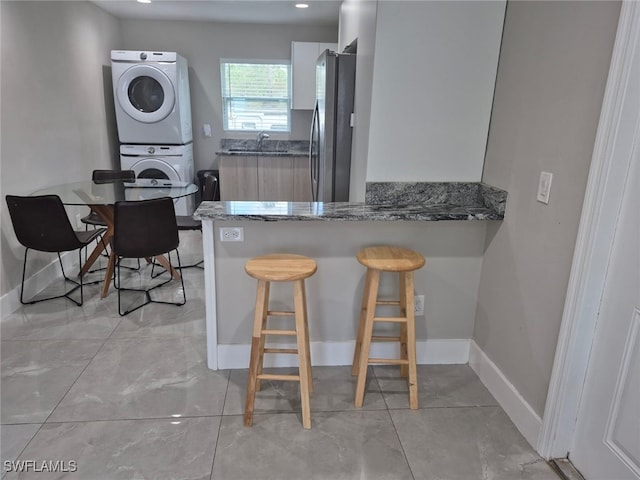 kitchen featuring stainless steel fridge, dark stone countertops, stacked washer / drying machine, white cabinets, and kitchen peninsula