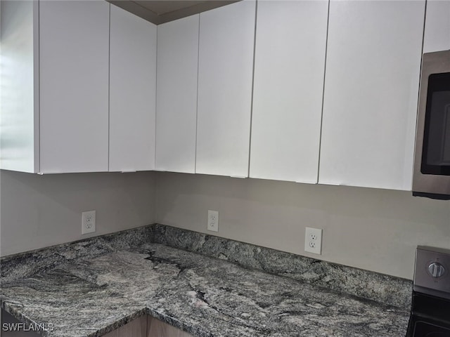 details with dark stone countertops, electric range oven, and white cabinets