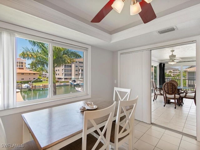 tiled dining area featuring crown molding, a tray ceiling, ceiling fan, and a water view