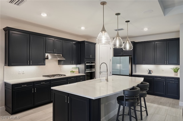 kitchen with sink, hanging light fixtures, a center island with sink, stainless steel appliances, and a kitchen bar