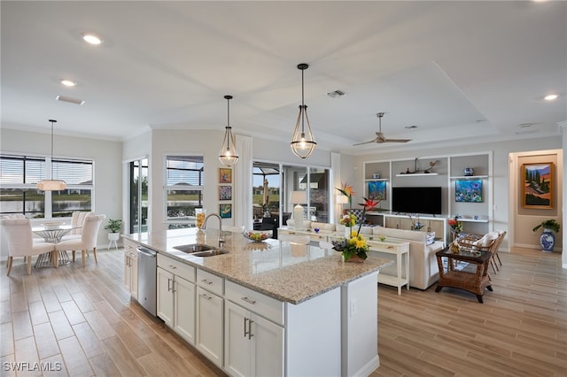 kitchen with sink, white cabinets, hanging light fixtures, light stone counters, and a center island with sink