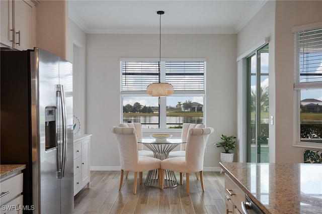 dining area with a water view, light hardwood / wood-style floors, and a wealth of natural light