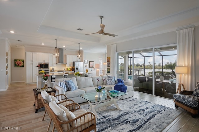 living room with crown molding, a tray ceiling, ceiling fan, and light wood-type flooring