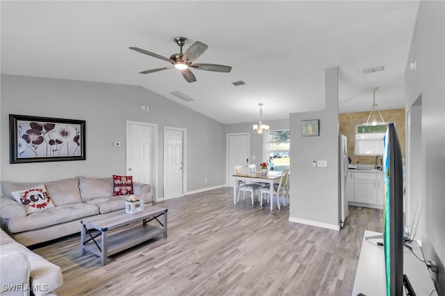 living room featuring vaulted ceiling, ceiling fan with notable chandelier, and light hardwood / wood-style floors