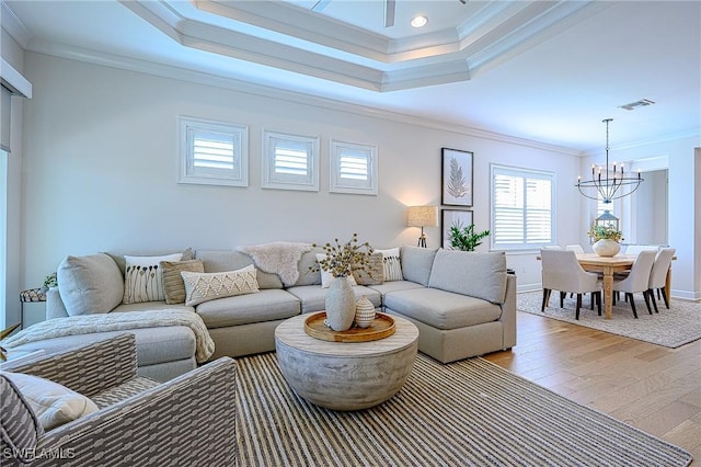 living room featuring crown molding, an inviting chandelier, light hardwood / wood-style floors, and a tray ceiling