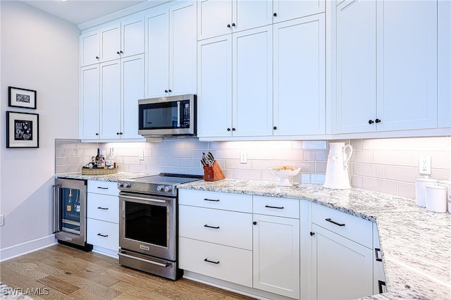 kitchen featuring appliances with stainless steel finishes, backsplash, wine cooler, light stone countertops, and white cabinets