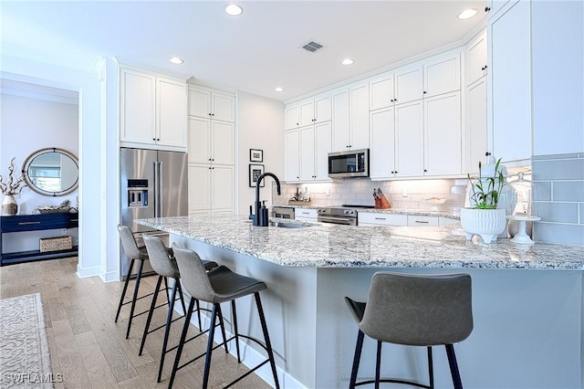 kitchen with sink, a breakfast bar area, white cabinets, backsplash, and stainless steel appliances