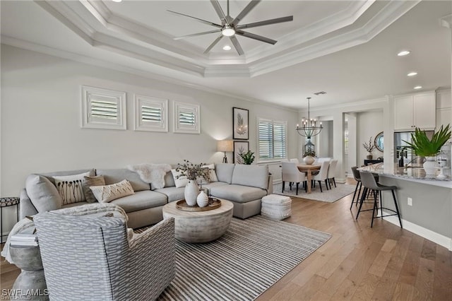 living room featuring ceiling fan with notable chandelier, ornamental molding, light hardwood / wood-style floors, and a raised ceiling