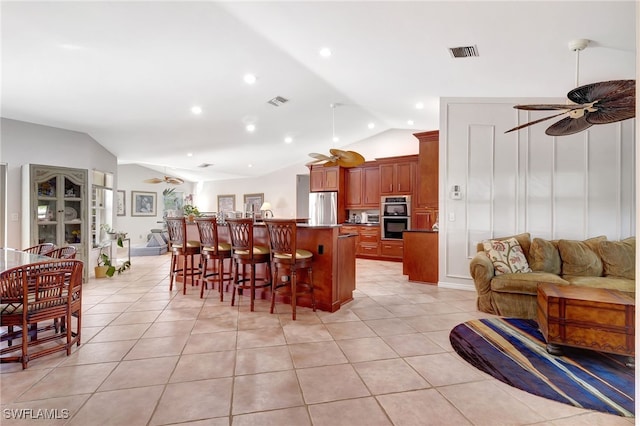 kitchen with vaulted ceiling, stainless steel appliances, a breakfast bar, and ceiling fan