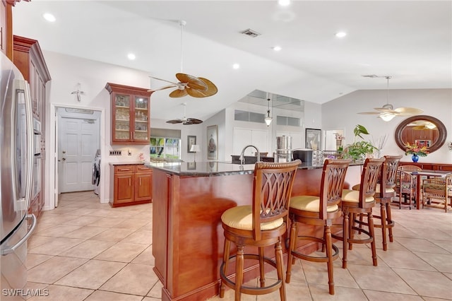 kitchen featuring light tile patterned flooring, lofted ceiling, a kitchen bar, dark stone countertops, and stainless steel fridge