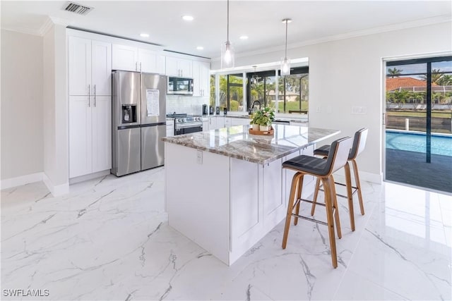 kitchen featuring light stone counters, a center island, ornamental molding, stainless steel appliances, and white cabinets