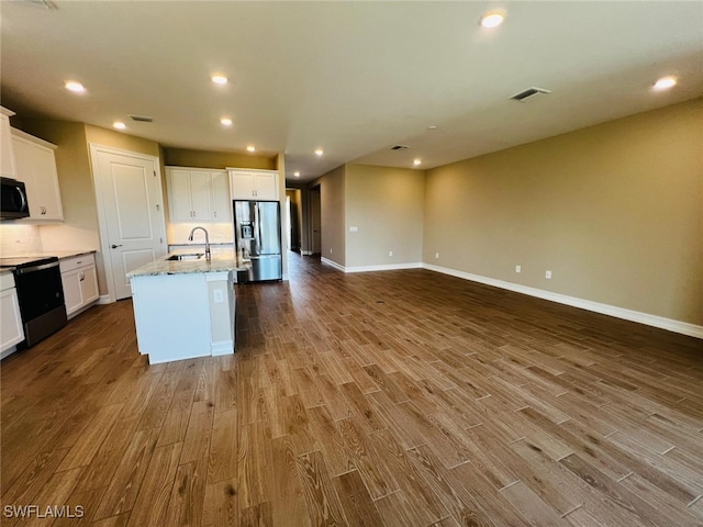 kitchen with sink, a kitchen island with sink, stainless steel refrigerator with ice dispenser, range with electric stovetop, and white cabinets