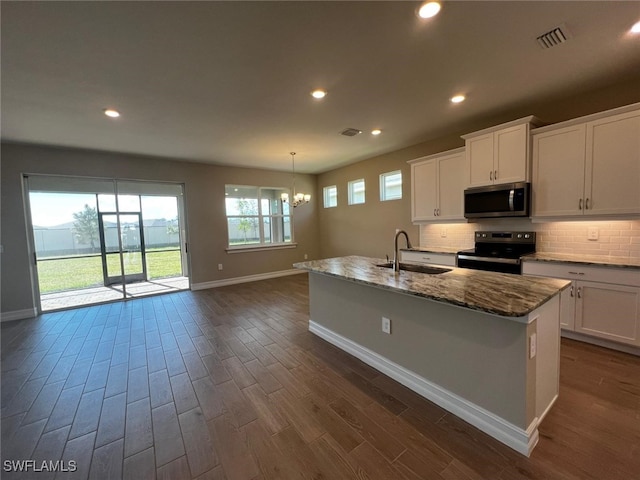 kitchen featuring white cabinetry, sink, dark stone countertops, a kitchen island with sink, and black / electric stove