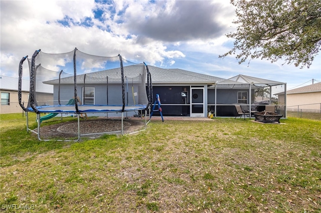 rear view of house with a trampoline, a fire pit, and a lawn