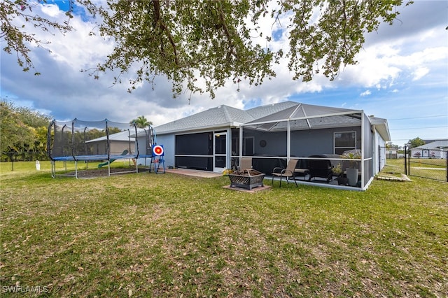 back of house featuring a lawn, glass enclosure, and an outdoor fire pit