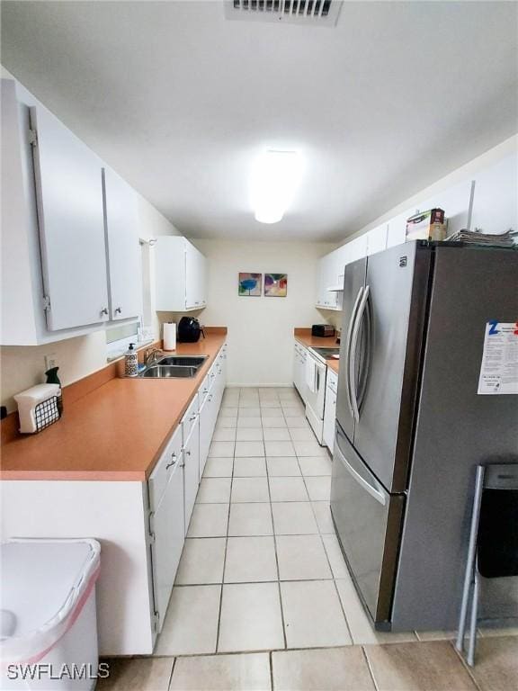 kitchen with white electric range, sink, light tile patterned floors, stainless steel fridge, and white cabinets