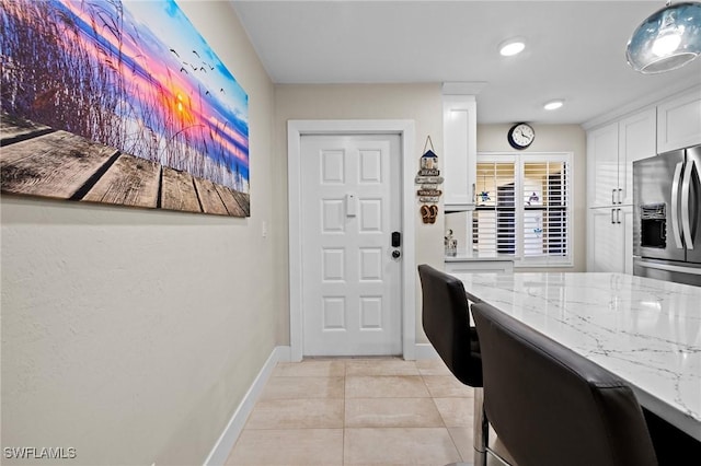 kitchen with white cabinetry, light tile patterned floors, stainless steel fridge, and light stone countertops