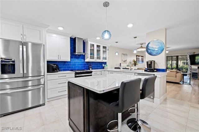 kitchen with wall chimney range hood, stainless steel appliances, white cabinets, a kitchen bar, and kitchen peninsula