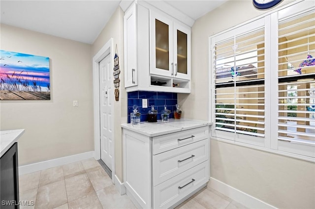 bar with white cabinetry, backsplash, light stone countertops, and light tile patterned flooring