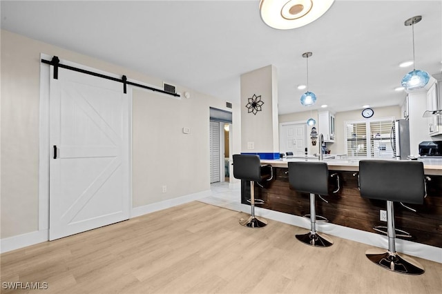 interior space featuring stainless steel refrigerator, white cabinets, a kitchen bar, decorative light fixtures, and a barn door