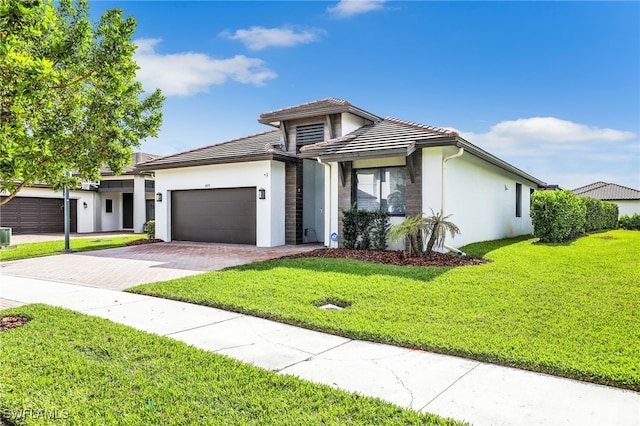 prairie-style house with a garage, decorative driveway, a front lawn, and stucco siding