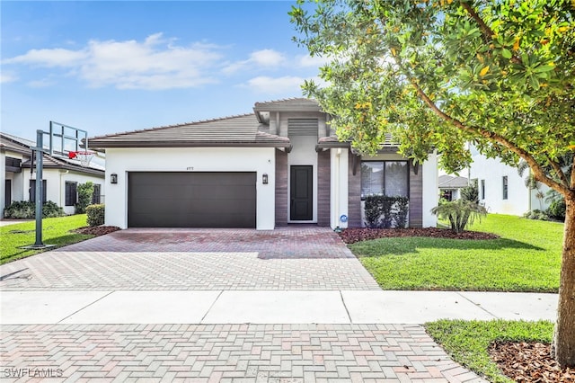 view of front facade featuring decorative driveway, a front lawn, a tiled roof, a garage, and stucco siding