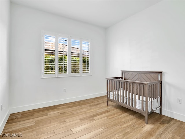 unfurnished bedroom with a nursery area, light wood-type flooring, and baseboards