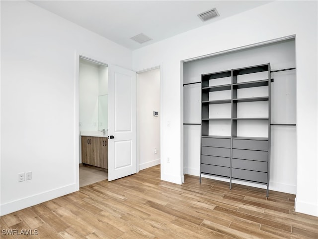unfurnished bedroom with light wood-style floors, visible vents, baseboards, and connected bathroom