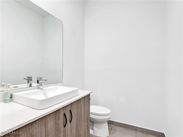 half bathroom with baseboards, tile patterned flooring, vanity, and toilet