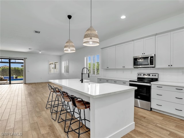 kitchen with a sink, light wood-type flooring, light countertops, appliances with stainless steel finishes, and visible vents