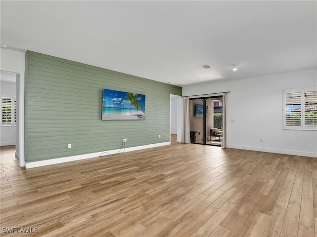 unfurnished living room with light wood-type flooring, a healthy amount of sunlight, and baseboards