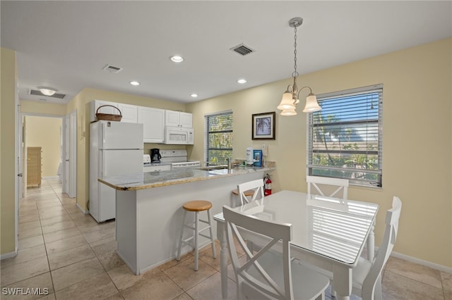 kitchen featuring white appliances, hanging light fixtures, white cabinets, a kitchen bar, and kitchen peninsula