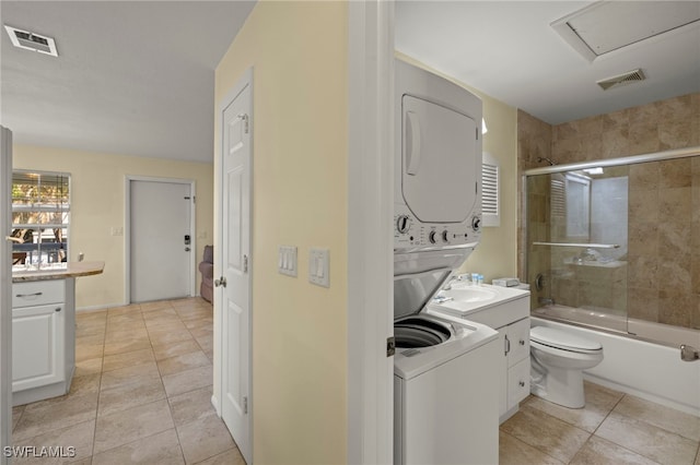 full bathroom featuring stacked washing maching and dryer, combined bath / shower with glass door, tile patterned flooring, vanity, and toilet