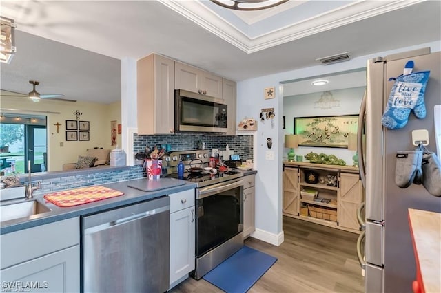 kitchen with appliances with stainless steel finishes, sink, decorative backsplash, ceiling fan, and light wood-type flooring