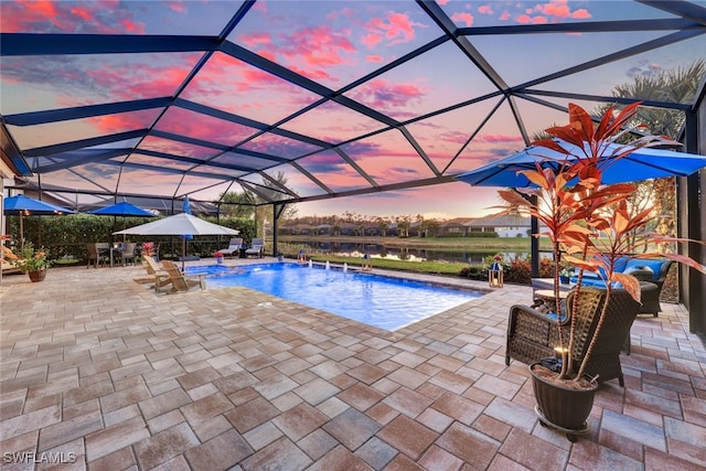 pool at dusk with pool water feature, a patio, a water view, and glass enclosure