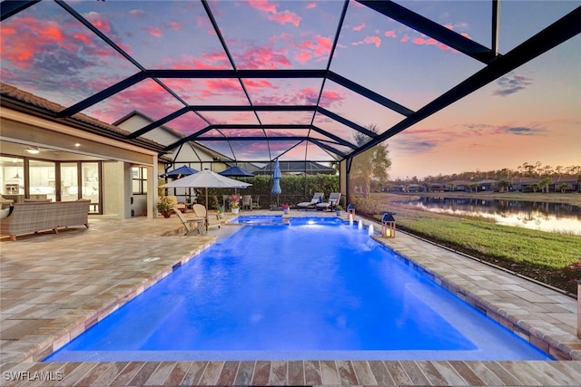 pool at dusk featuring pool water feature, a water view, a hot tub, a lanai, and a patio