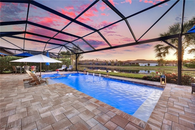 pool at dusk with a water view, a patio area, and glass enclosure