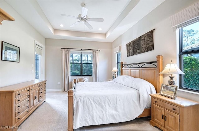 bedroom featuring multiple windows, a tray ceiling, light colored carpet, and ceiling fan