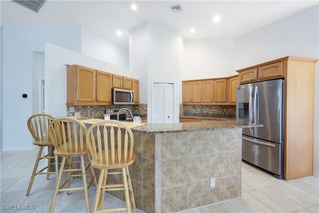 kitchen featuring a kitchen island with sink, a breakfast bar area, stone counters, and appliances with stainless steel finishes