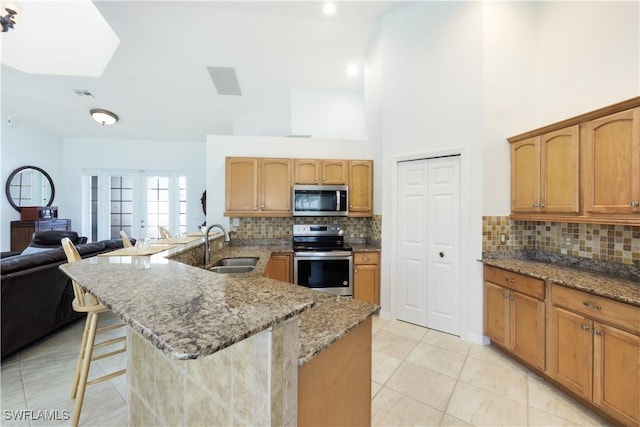 kitchen featuring a kitchen bar, sink, light stone counters, stainless steel appliances, and decorative backsplash