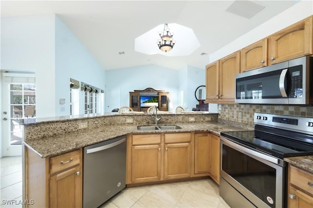 kitchen with sink, stainless steel appliances, kitchen peninsula, vaulted ceiling, and dark stone counters