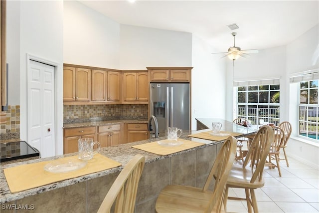 kitchen featuring tasteful backsplash, stainless steel fridge, high vaulted ceiling, and light tile patterned floors