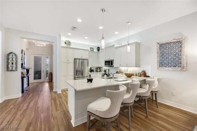 kitchen featuring appliances with stainless steel finishes, pendant lighting, tasteful backsplash, white cabinetry, and a kitchen breakfast bar